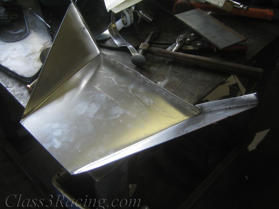 Folded bare sheet-metal fabricated part resting on a metal workbench with hammers and tools