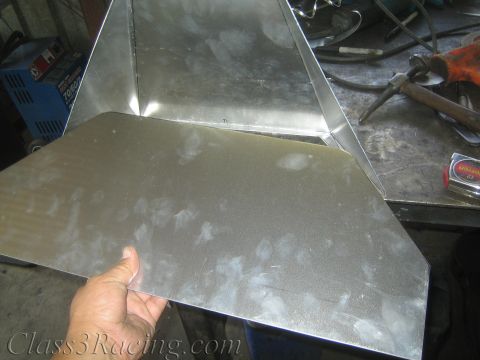 1990 Ford Bronco - hand holds a large folded bare sheet-metal panel on a steel bench near a grinder, hammer, and other shop tools.