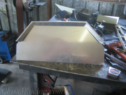 1990 Ford Bronco - folded bare sheet-metal tray-shaped fabricated part rests on a steel workbench surrounded by hammers and hand tools.