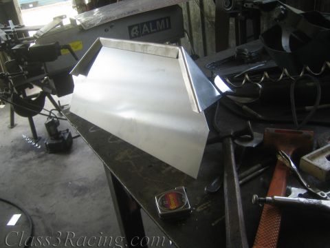 1990 Ford Bronco - folded bare sheet-metal part rests on a steel bench beside an ALMI metal bender, a tape measure, and hand tools.