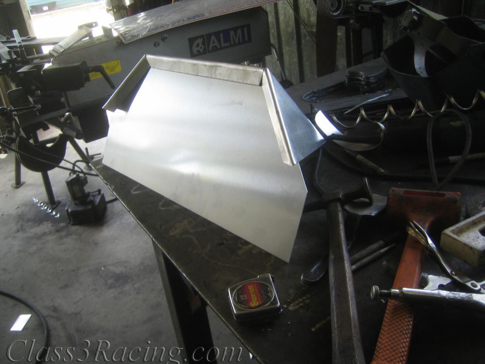 Fabricated bare sheet-metal part on a bench beside an ALMI bending machine in a shop
