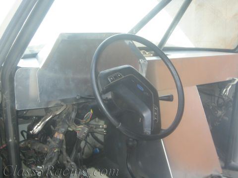 1990 Ford Bronco - Gutted truck cabin showing a Ford steering wheel beside an unpainted aluminum dash panel over exposed wiring.