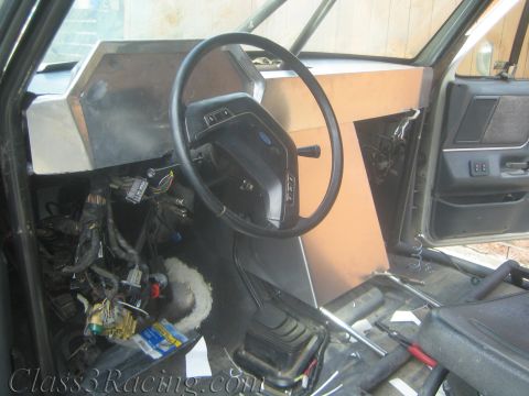 1990 Ford Bronco - Ford steering wheel beside an unpainted aluminum dash panel above a tangle of exposed wiring in a gutted vehicle.
