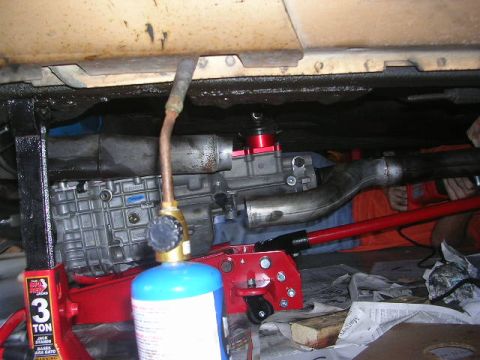 1975 Ford Ranchero - Close-up view of a vehicle's transmission and exhaust system, supported by jack stands and a hydraulic jack.