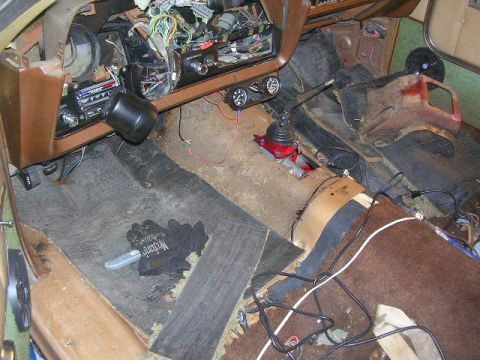 1975 Ford Ranchero - The interior of a vehicle shows exposed wiring, a manual transmission shifter, and significant wear on the carpeting and dashboard.