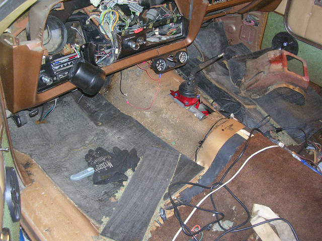 Vehicle interior with exposed wiring, manual shifter, and worn carpeting