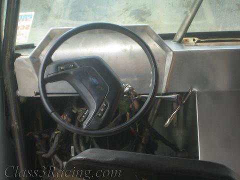 1990 Ford Bronco - Ford steering wheel attached to a bare aluminum dash panel inside a stripped vehicle cabin.