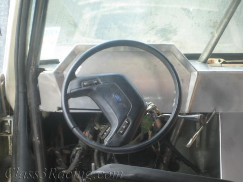 1990 Ford Bronco - Front view of a Ford steering wheel and unpainted aluminum dashboard above exposed wiring in a gutted vehicle.