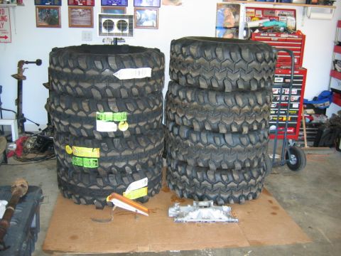1992 Ford Mustang - Several large off-road tires are stacked in a garage next to a red tool chest and an engine part.