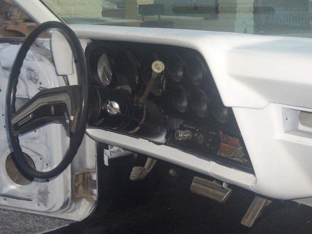 White car interior with bare dash showing empty gauge holes and black steering wheel