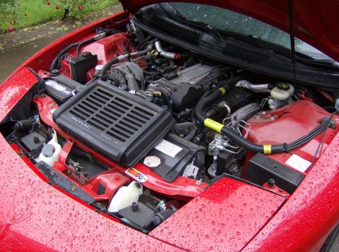 1996 Pontiac Trans Am - The engine bay of a red 1996 Pontiac Trans Am is visible with the hood open, revealing the V8 engine and air intake system.