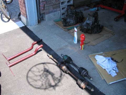 1993 Ford Probe - Various automotive parts are laid out on a driveway, possibly for repair or replacement.
