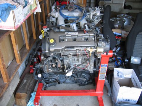 1993 Ford Probe - A Mazda engine is mounted on a red stand, surrounded by garage clutter and car parts.