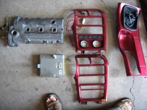 1993 Ford Probe - Various car parts including an engine valve cover and ECU are displayed on a concrete surface.