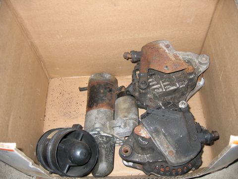 1993 Ford Probe - A collection of automotive parts, including starters and an alternator, are stored in a cardboard box.