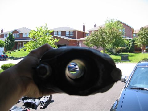 1993 Ford Probe - A dark exhaust pipe part is held in the foreground, with a blue car visible through its central opening.