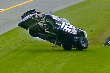 1981 Ford Bronco - Stock car number 12 has crashed and is on its side on a grassy slope next to a track.