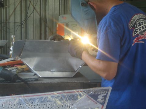 1990 Ford Bronco - worker in a blue T-shirt welds an aluminum fabrication, the arc throwing a bright flare in the workshop.