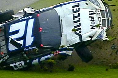 1981 Ford Bronco - A race car lies overturned on a grassy area, its wheels in the air.