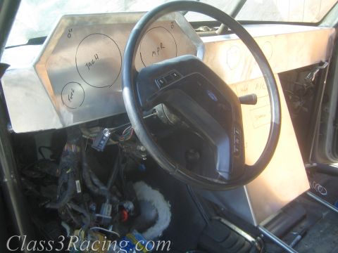 1990 Ford Bronco - black steering wheel and bare aluminum dash with penciled circular gauge layouts in a gutted race vehicle cab.