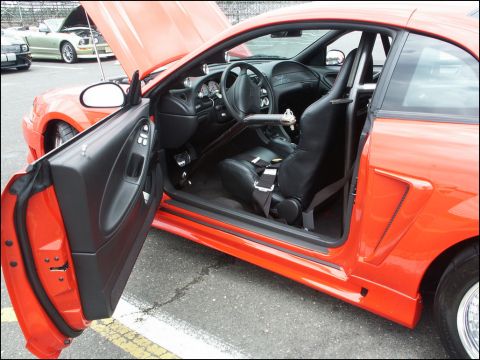 2001 Mercury Grand Marquis - Interior view of an orange sports car with racing seat and roll cage, parked at an outdoor event.