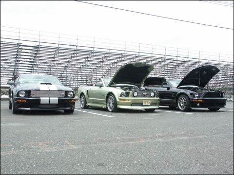 2001 Mercury Grand Marquis - Three Ford Mustangs are parked in a lot with stadium seating in the background.