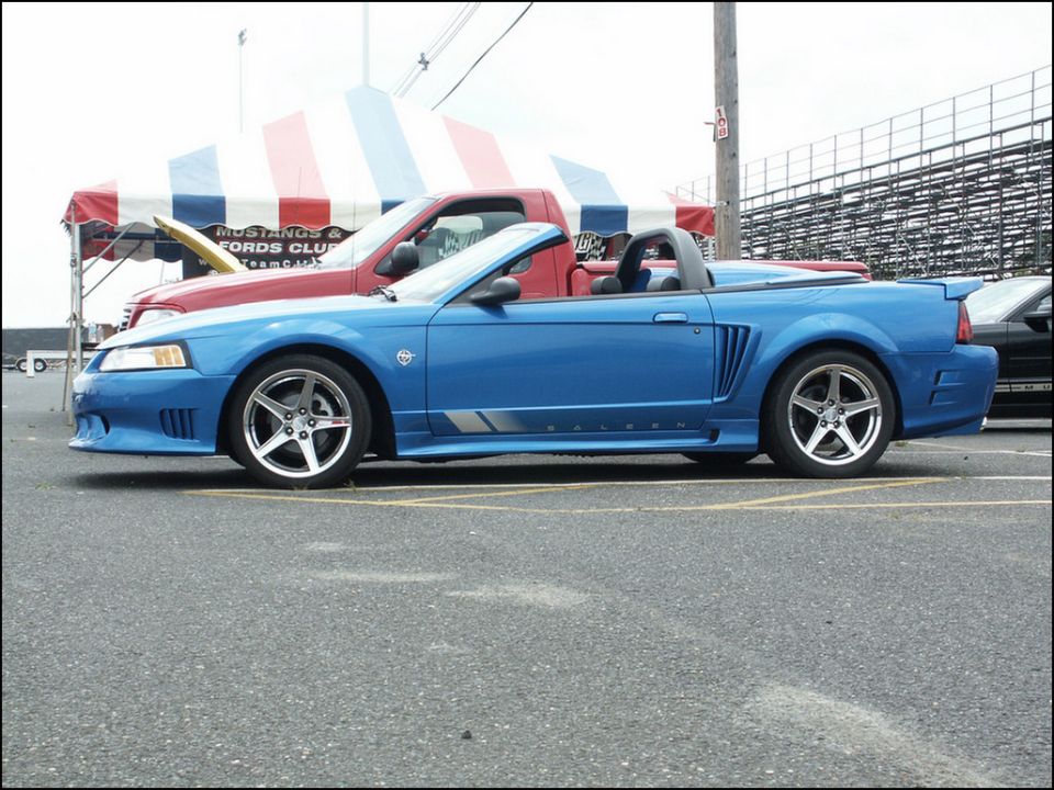 Blue convertible sports car with silver stripe on rocker panel. Red truck behind it