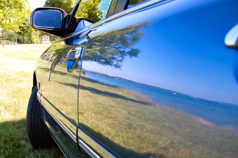 1985 Mercury Grand Marquis - A blue car is parked on a grassy area, with reflections visible on its side.
