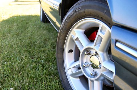 1985 Mercury Grand Marquis - A close-up shot focuses on the wheel and fender of a car, with grass visible in the background.