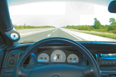 1985 Mercury Grand Marquis - Interior view of a car dashboard with a steering wheel and gauges, looking out at a highway.