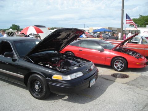1992 Ford Crown Victoria - A black 1992 Ford Crown Victoria is parked with its hood open at a car show, alongside other vehicles.