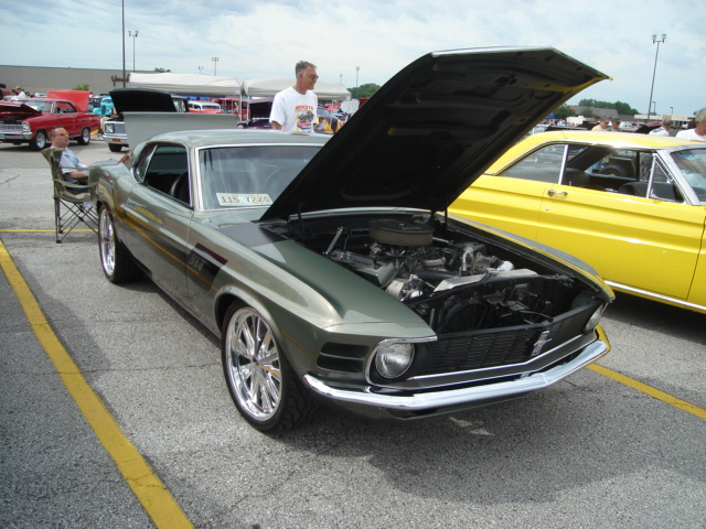 Green 1969 Ford Mustang Boss 302 with hood open, parked next to a yellow car