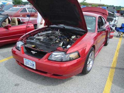 1992 Ford Crown Victoria - A red Ford Mustang is displayed with its hood open, revealing the engine compartment. Other vehicles are parked nearby.