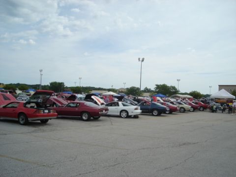 1992 Ford Crown Victoria - A variety of vehicles are displayed at an outdoor car show, with many hoods open to reveal engines.