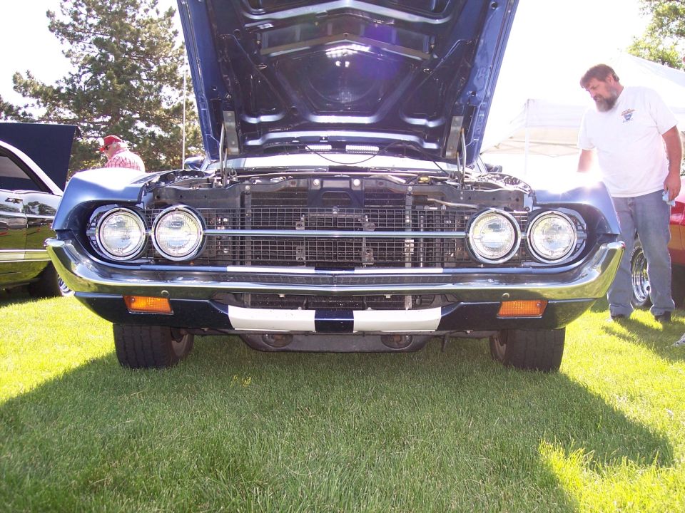 Front view of a blue 1969 Ford Torino GT with hood open, parked on grass at an outdoor event