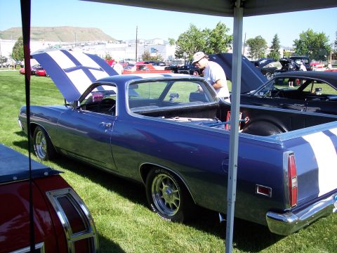 1972 Ford Ranchero - A blue 1972 Ford Ranchero with distinctive white racing stripes is displayed at a car show, with its hood open.