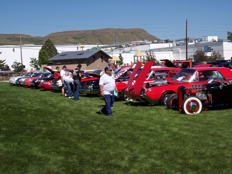 Row of classic cars with hoods up at an outdoor car show. One red 1972 Ford Ranchero is visible