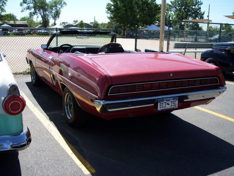 1972 Ford Ranchero - A red convertible is parked next to another vehicle, showing its rear end and license plate.