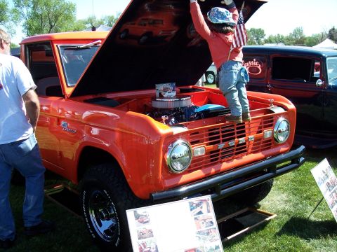 1972 Ford Ranchero - Child stands on the grille of an orange Ford Bronco with its hood open at a car show.