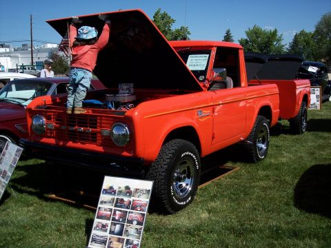 1972 Ford Ranchero - A child peers into the engine bay of an orange 1972 Ford Bronco at a car show, with another Bronco visible in the background.