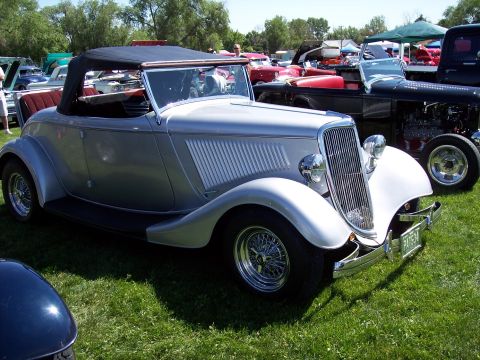 1972 Ford Ranchero - Silver 1934 Ford hot rod convertible parked on grass at a car show, with other vehicles in the background.