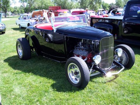 1972 Ford Ranchero - A classic black hot rod roadster is displayed on a grassy field at an outdoor event with other vehicles present.