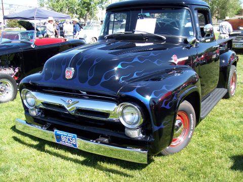 1972 Ford Ranchero - A black pickup truck with custom blue flame paint and red wheels is parked on grass at an outdoor event.
