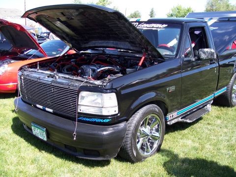 1972 Ford Ranchero - A black Ford F-150 Lightning pickup truck is displayed with its hood open, revealing the engine bay.