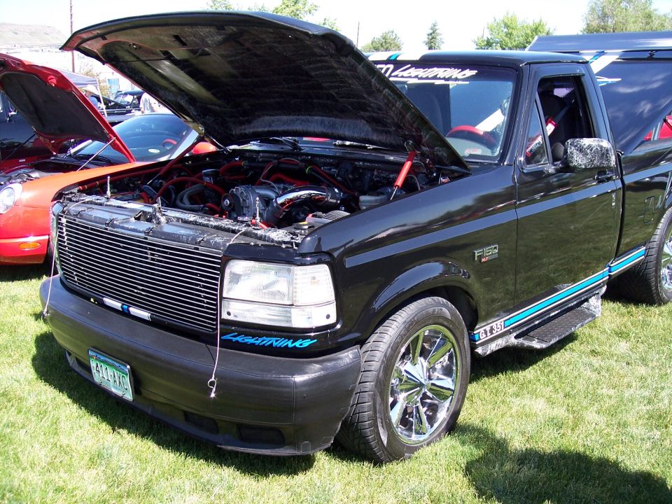 Black Ford F-150 Lightning pickup truck with hood open, chrome wheels, and blue racing stripes