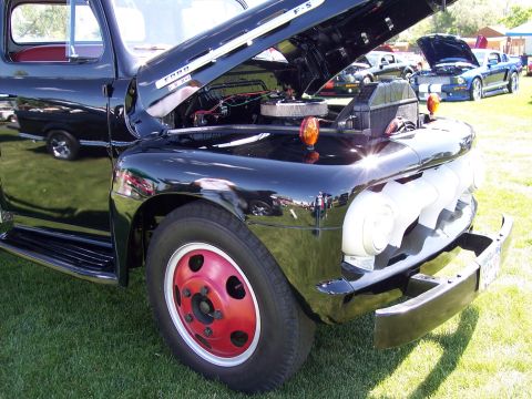 1972 Ford Ranchero - A black Ford F-5 truck is displayed with its hood open, revealing the engine compartment. Other vehicles are visible in the background.