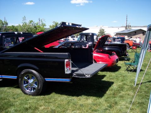 1972 Ford Ranchero - Several vehicles are parked on a grassy field under a sunny sky, with one truck's tailgate and tonneau cover open.
