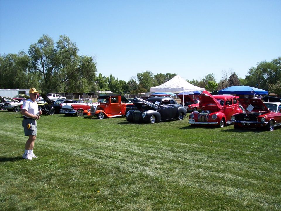 Man in yellow hat stands on grass near several classic cars with hoods up