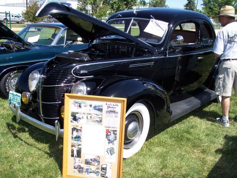 1972 Ford Ranchero - A man in a hat looks at a black 1939 Ford Coupe at an outdoor car show.