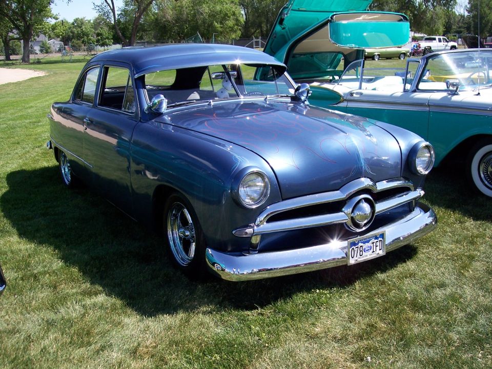 1950 Ford Custom sedan with custom paint and chrome wheels, parked on grass next to another classic car